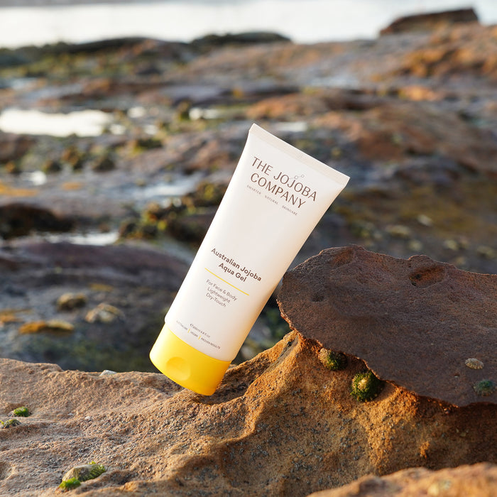 Tube of The Jojoba Company sunscreen on a rock with ocean background