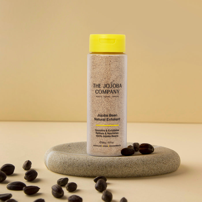 Bottle of The Jojoba Company product on a beige background with jojoba beans around