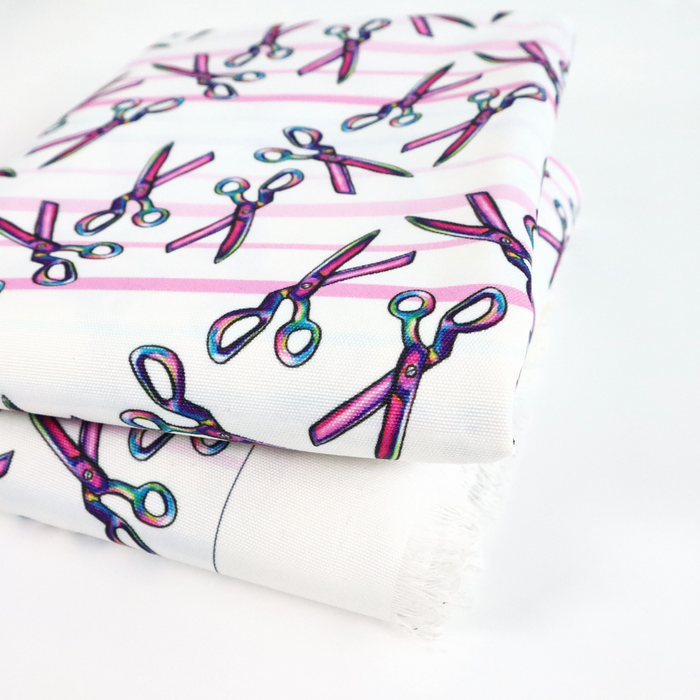 This ReNew Canvas print is of a rainbow scissors design over light blue, pink, and white stripes. This photo is of the fabric folded.
