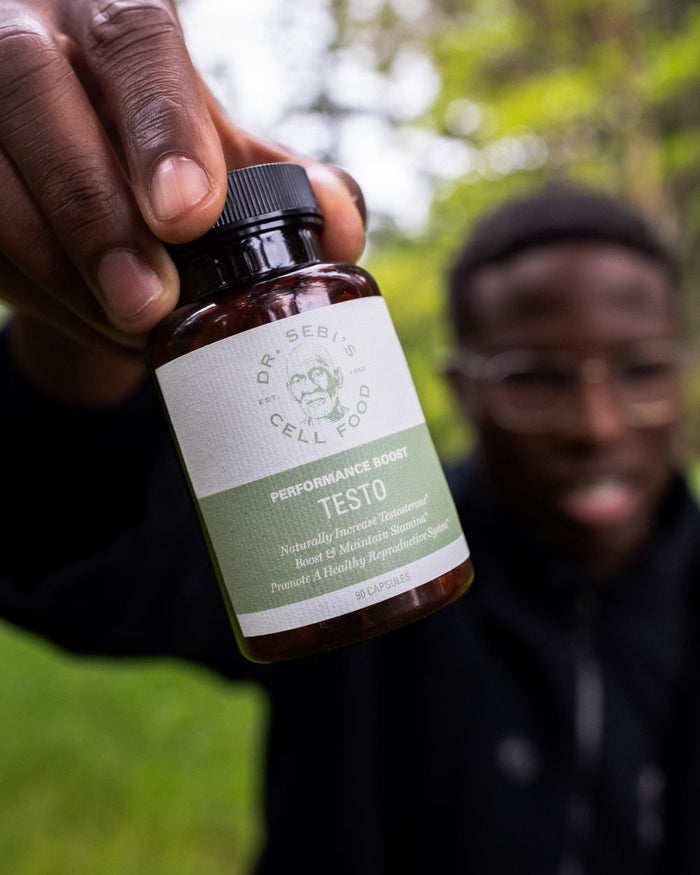 Hand holding Dr. Sebi's Performance Boost Testo supplement bottle outdoors in natural green setting.