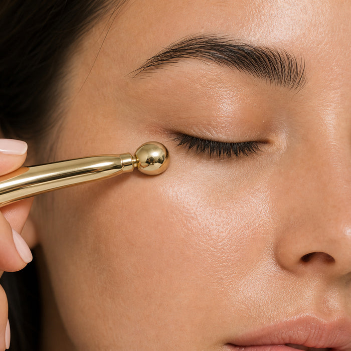 Close-up of a person's face with a gold facial roller tool being used under the eye.