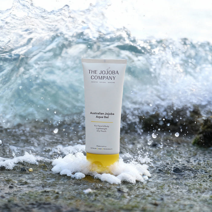 Tube of The Jojoba Company product on a beach with waves in the background