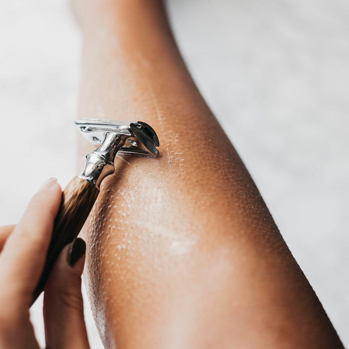 Close up of a bamboo safety razor gliding over a forearm with shaving foam.
