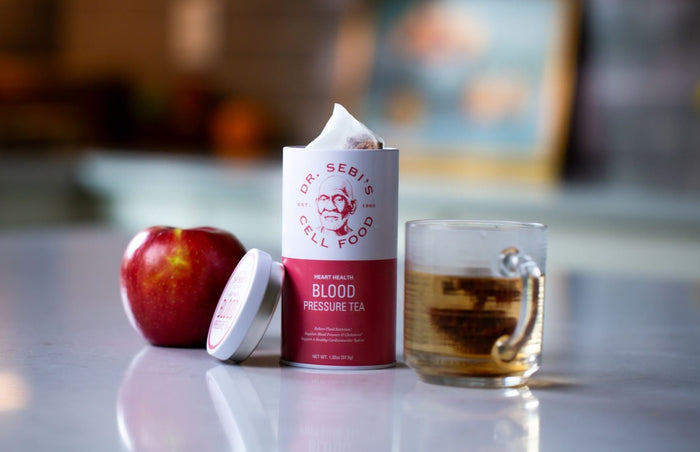 Dr. Sebi's Blood Pressure Tea with red apple and brewed tea cup on marble surface.