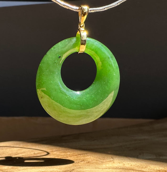 Green jade pendant on a chain against a dark background