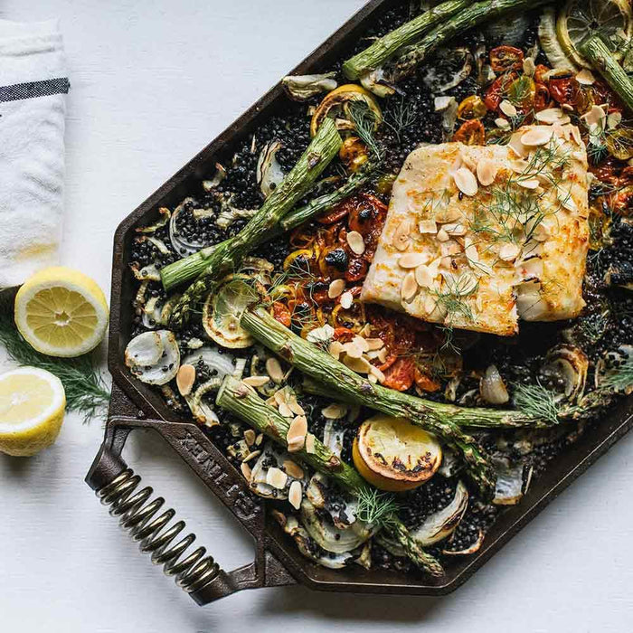 FINEX 18″ Double Burner Cast Iron Griddle with cooked veggies and fish displayed on a white tabletop