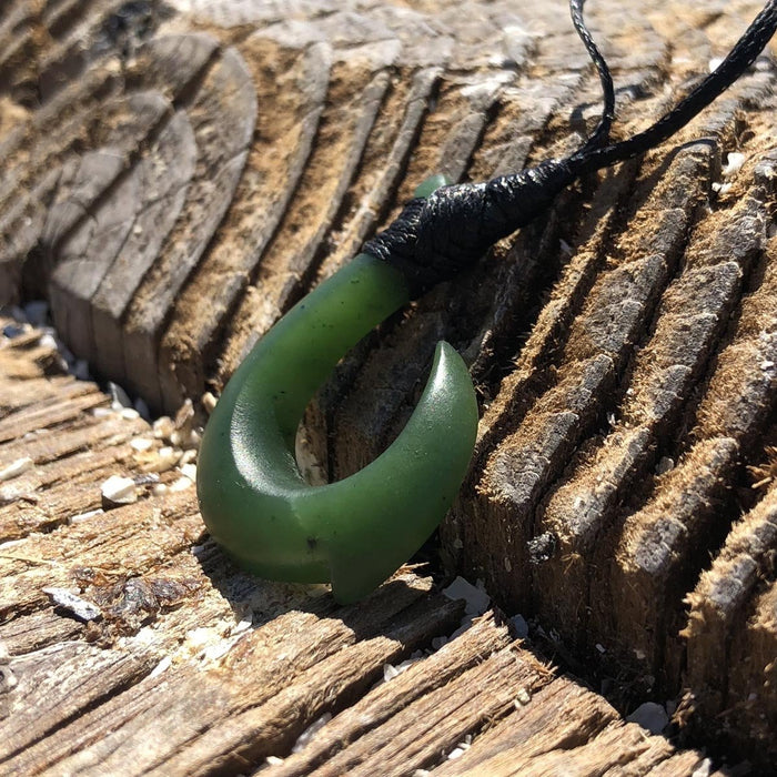 Side view of a green jade hook pendant tied with a black cord on weathered wood