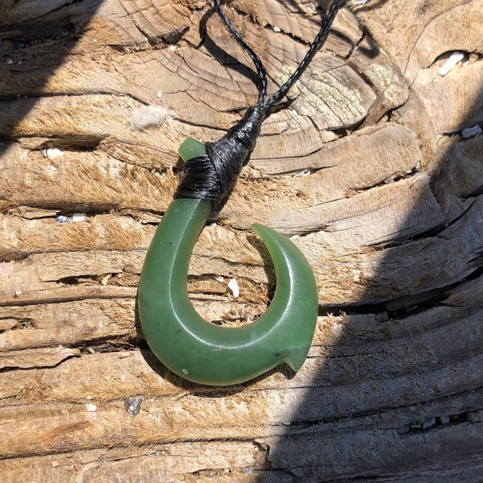Green jade hook pendant with a wrapped black cord on a weathered wood surface