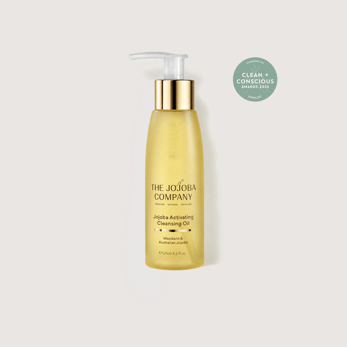 A bottle of The Jojoba Company Jodiba Activating Cleansing Oil in a translucent golden-yellow bottle with a gold pump and white cap, shown on a light gray background with a green award badge in the upper right.
