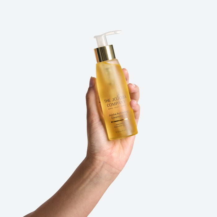 Hand holding a bottle of 'The Jojoba Company' Activating Cleansing Oil against a white background