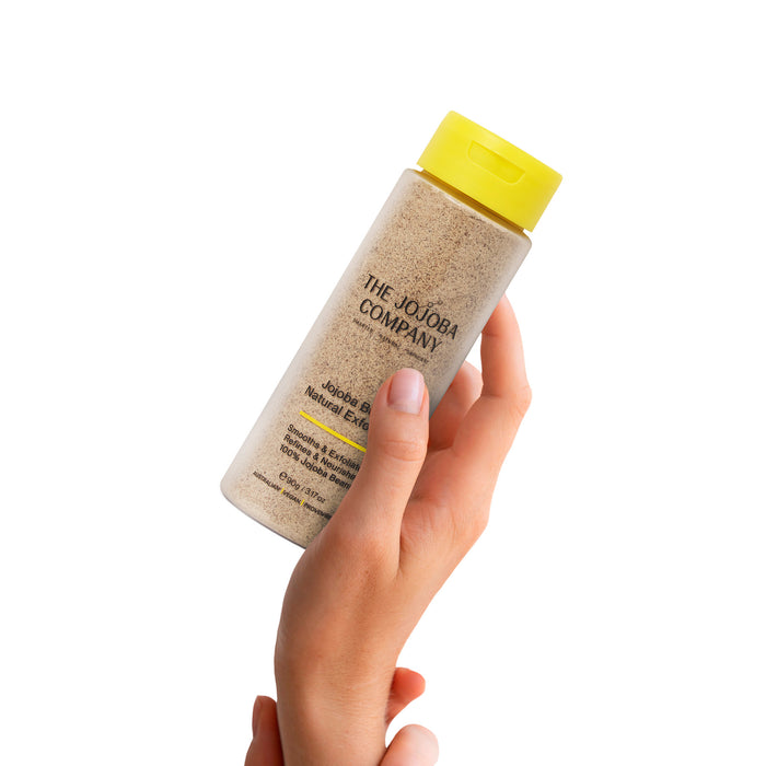 Hand holding a bottle of The Jojoba Company product with a yellow cap on a white background