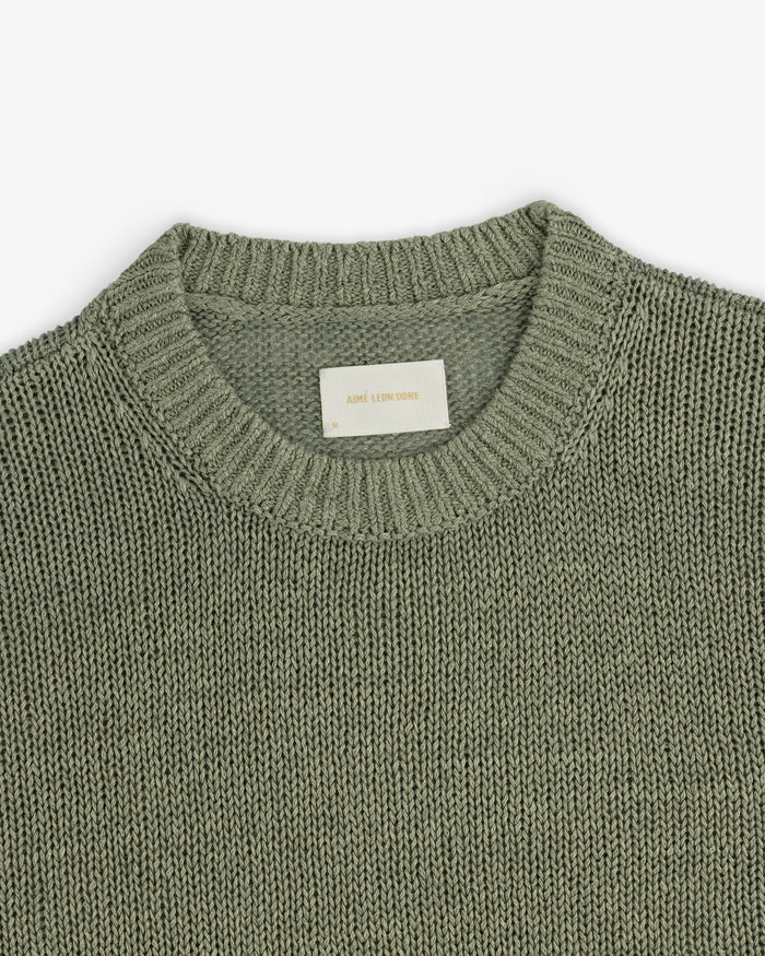 A close-up of the Linen Knit Crewneck Sweater in sage green, featuring a ribbed neckline and white inner label.