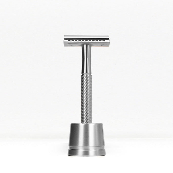 Silver metal double edge razor on a matching silver stand against a white background