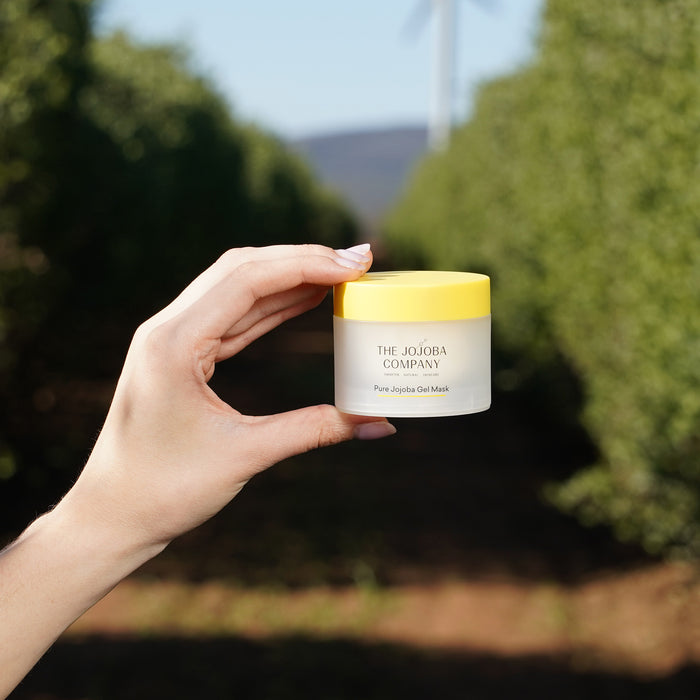 Hand holding a jar of 'The Jojoba Company' Pure jojoba Gel Mask product with a blurred outdoor background