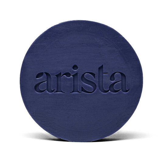 Deep blue circular shampoo bar with arista logo embossed on its surface