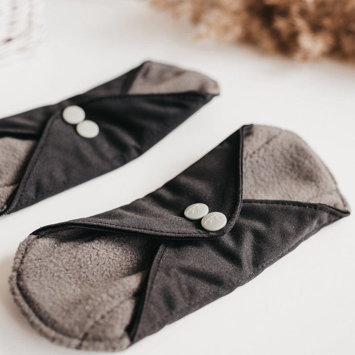 Close-up of two black reusable panty liners with gray interior and silver snaps.
