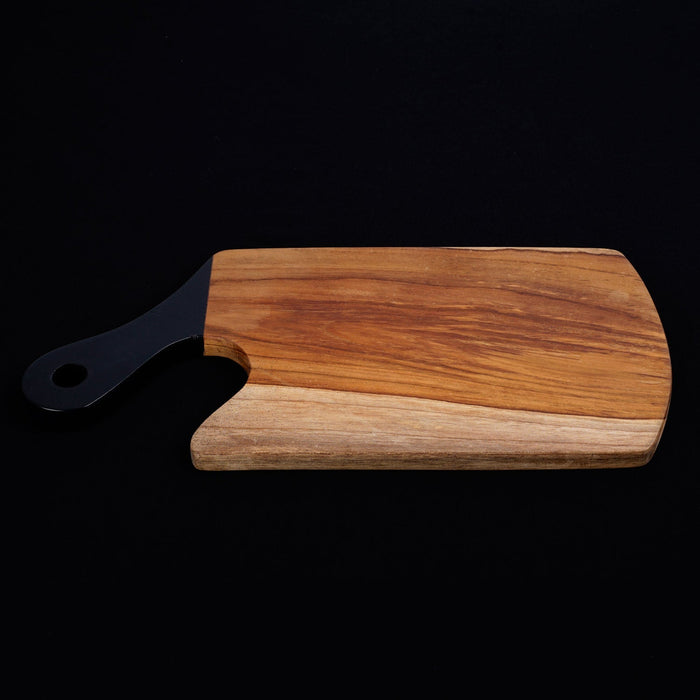 Teak cutting board with black handle displayed horizontally on a black background