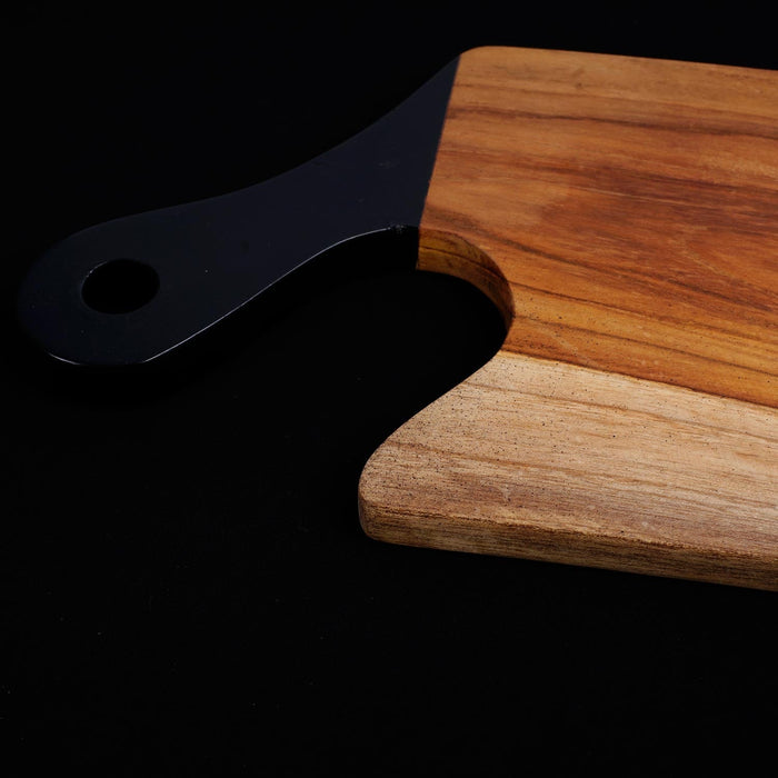 Close up of black handle of teak cutting board displayed on a black background