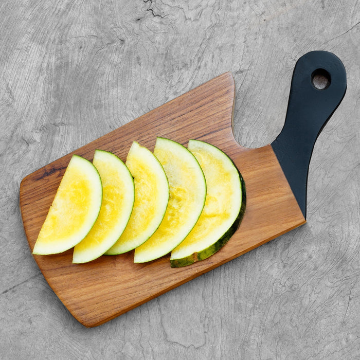 Top view of teak cutting board with black handle with sliced melon displayed on a wooden surface