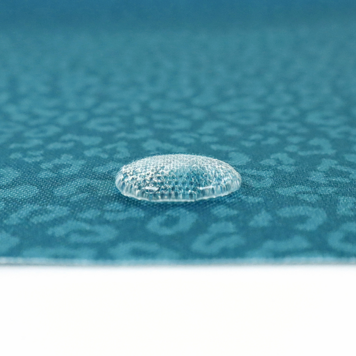 This printed WPC-Lite has a repeating light teal leopard print design with a deep saturated teal background. This photo shows a water drop on the fabric.