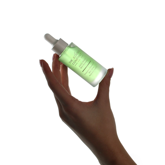 Hand holding a bottle of green serum against a white background
